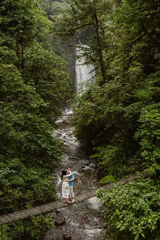 Couple kissing on a hanging bridge with El Tigre Waterfall in the background.