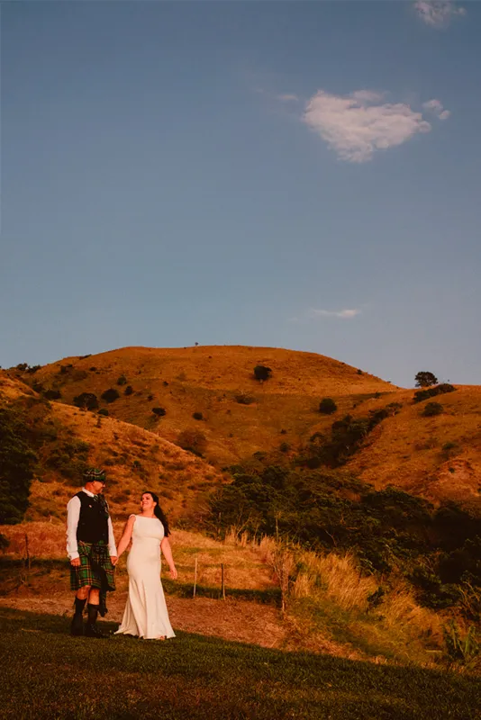 Couple walking hand in hand with sunset light and a reddish mountain behind them in Monteverde.