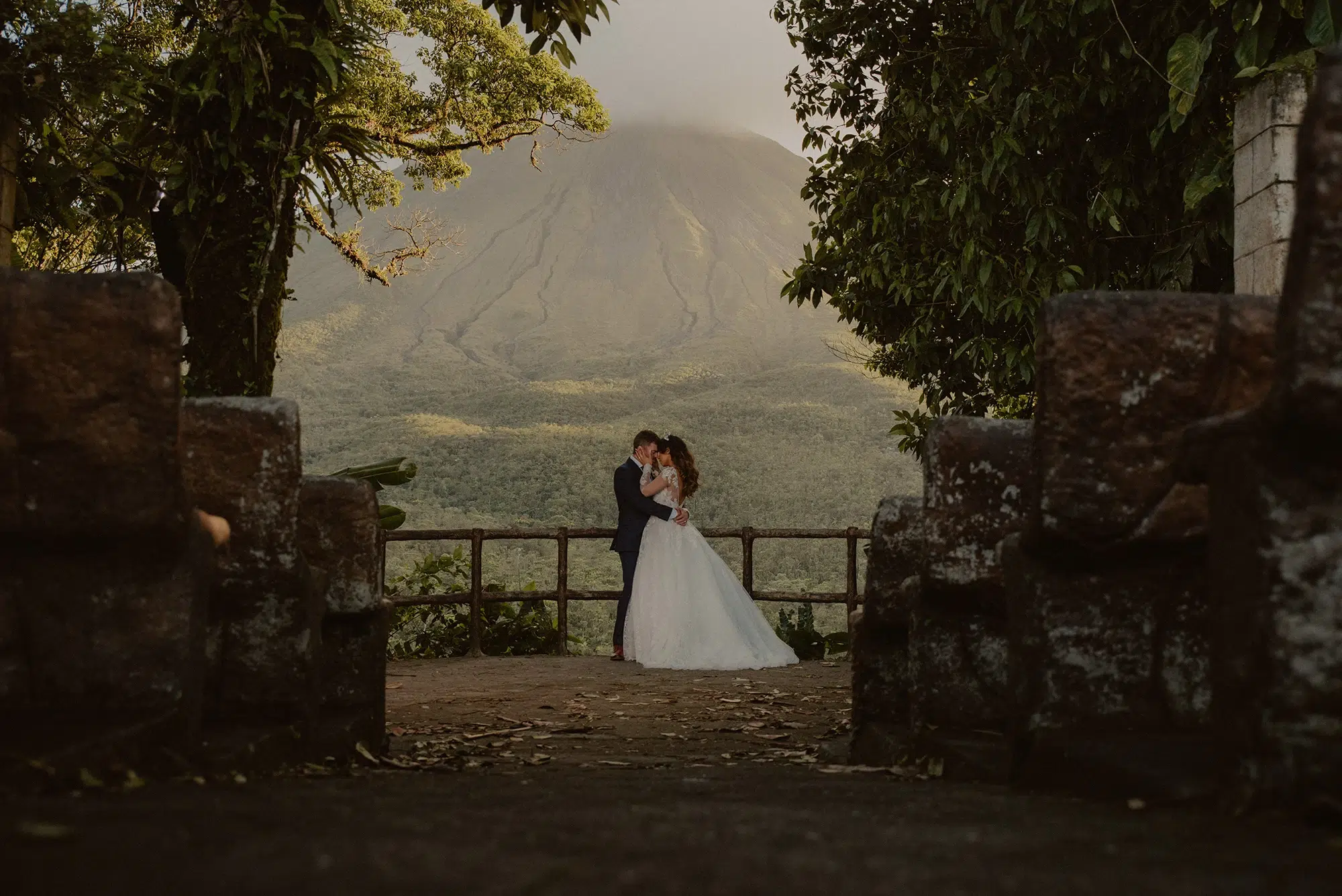 Couple standing on a viewpoint with the Arenal Volcano behind them.