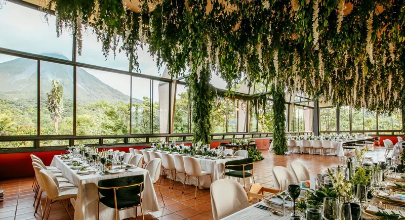 Wedding reception with hanging greenery and floor-to-ceiling windows facing Arenal Volcano at Arenal Kioro, La Fortuna, Costa Rica