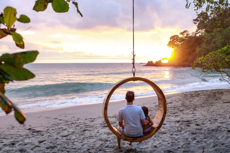 Couple sitting on a hanging ring swing on the beach at sunset at Arenas del Mar Resort, Manuel Antonio, Costa Rica