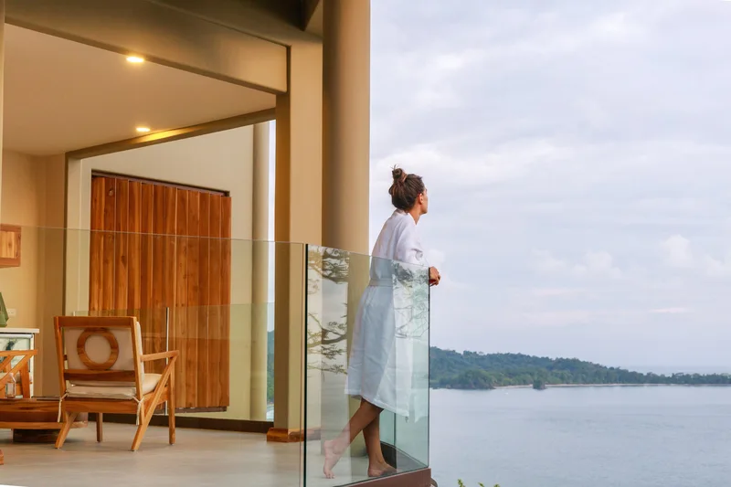 Woman in a white robe on a glass balcony overlooking the ocean at Arenas del Mar Resort, Manuel Antonio, Costa Rica