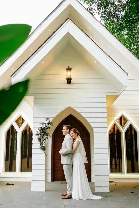 Bride and groom embracing at the door of a white wooden chapel at Casa del Río, La Fortuna, Costa Rica