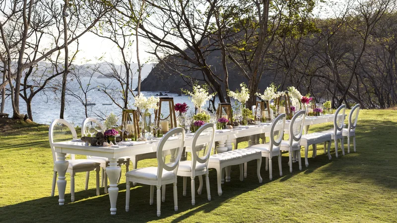 Outdoor wedding reception table with white chairs on a lawn overlooking the bay at Four Seasons Resort Costa Rica, Guanacaste