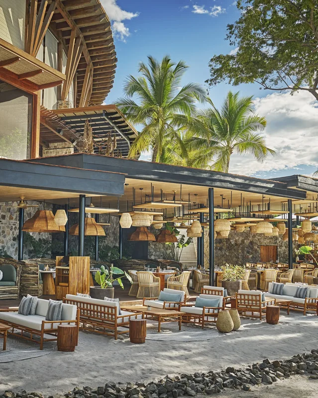 Open-air restaurant terrace with rattan lamps and lounge seating under palm trees at Four Seasons Resort Costa Rica, Guanacaste