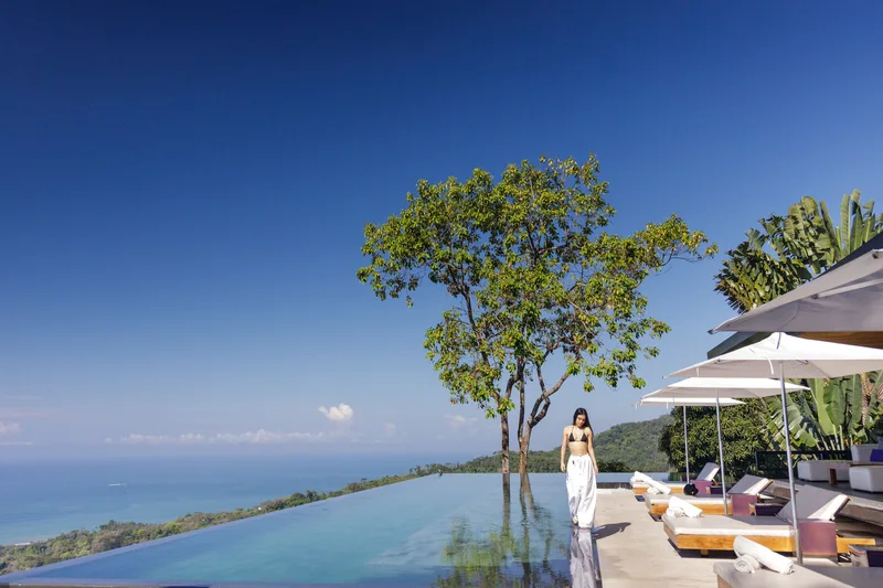 Woman in a white dress walking along the infinity pool with ocean views at Kura Boutique Hotel, Uvita, Costa Rica