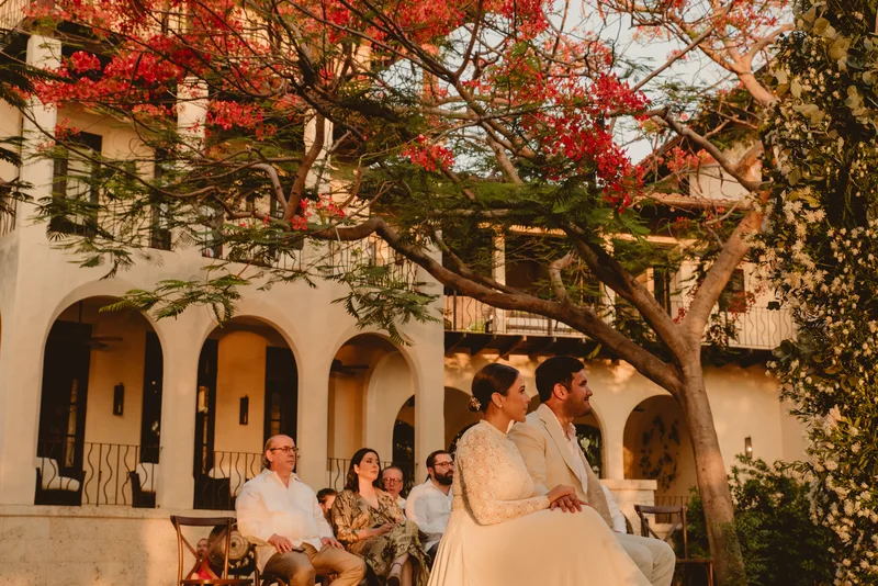 Couple at their wedding ceremony under a red flame tree with Las Catalinas' Spanish-colonial arches behind them