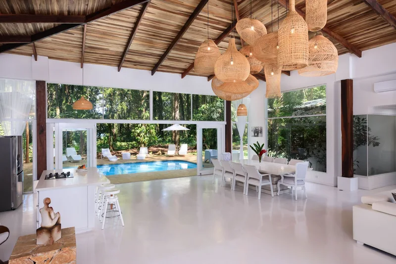 White villa living and dining area with rattan pendant lamps opening onto the pool at Le Caméléon, Puerto Viejo, Costa Rica