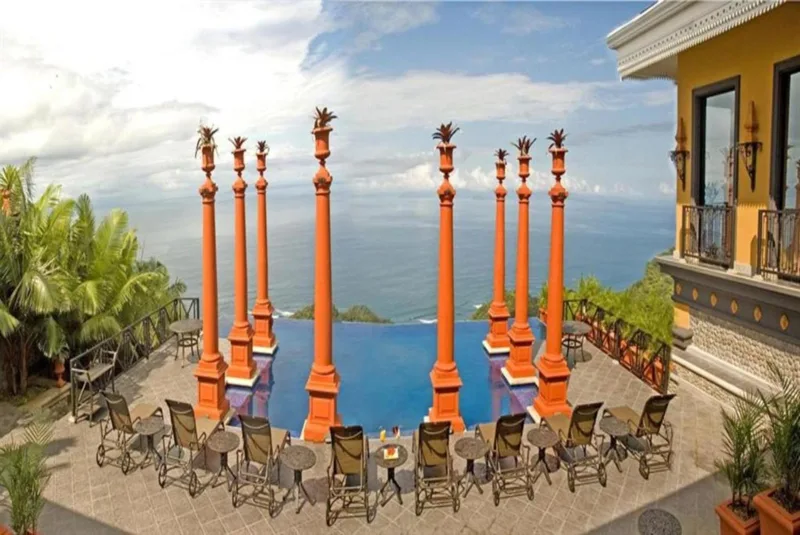 Chairs set around the infinity pool framed by tall orange columns overlooking the ocean at Villa Caletas wedding venue in Jacó, Costa Rica