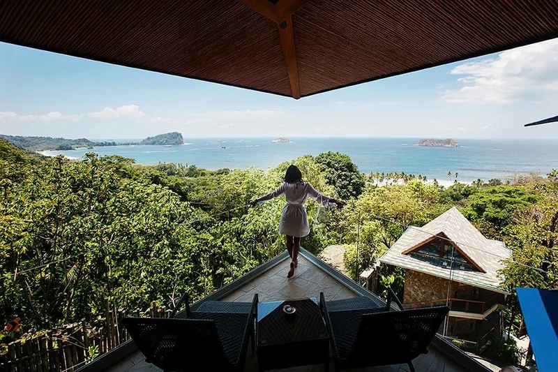 Woman with open arms on a rooftop terrace overlooking the rainforest and Manuel Antonio bay at Villa Punto de Vista, Costa Rica